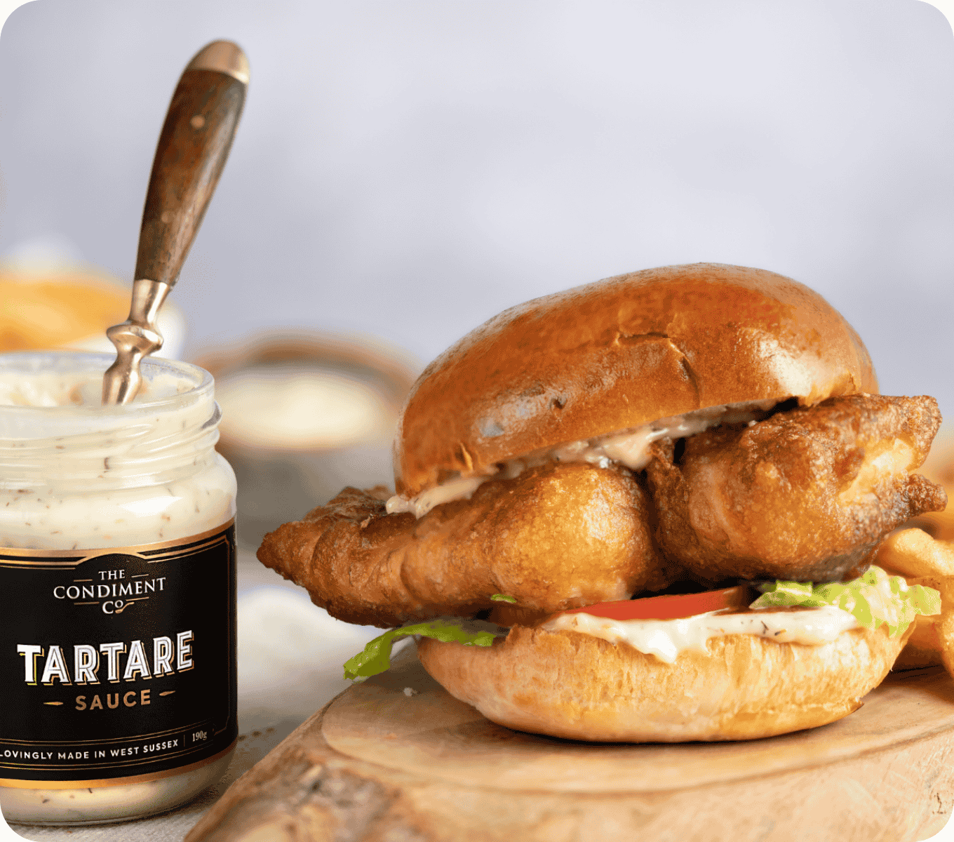 A jar of tartare sauce next to a fried fish sandwich